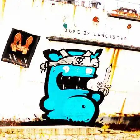 A bright blue cartoon monster with sharp teeth drinking from a cup painted as street art.